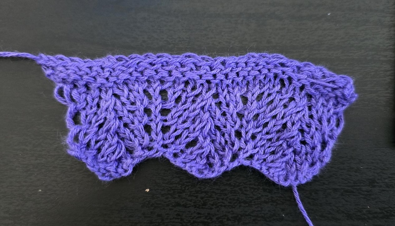 A short three-time repeat of a lace pattern, knitted in purple yarn.